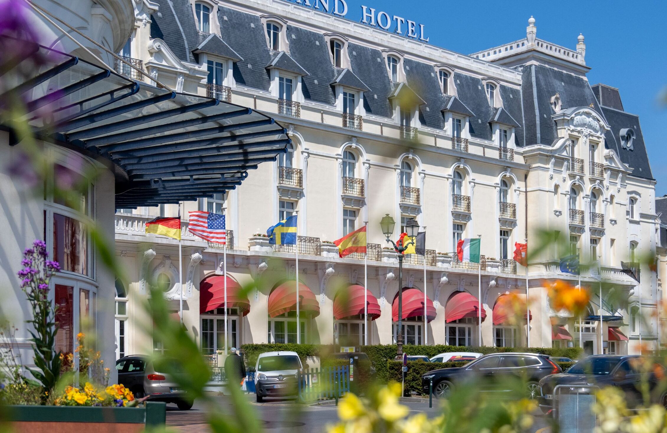 Ein imposantes Hotel im klassischen Stil, mit mehreren Flaggen, einer überdachten Eingangshalle und einem Parkplatz.