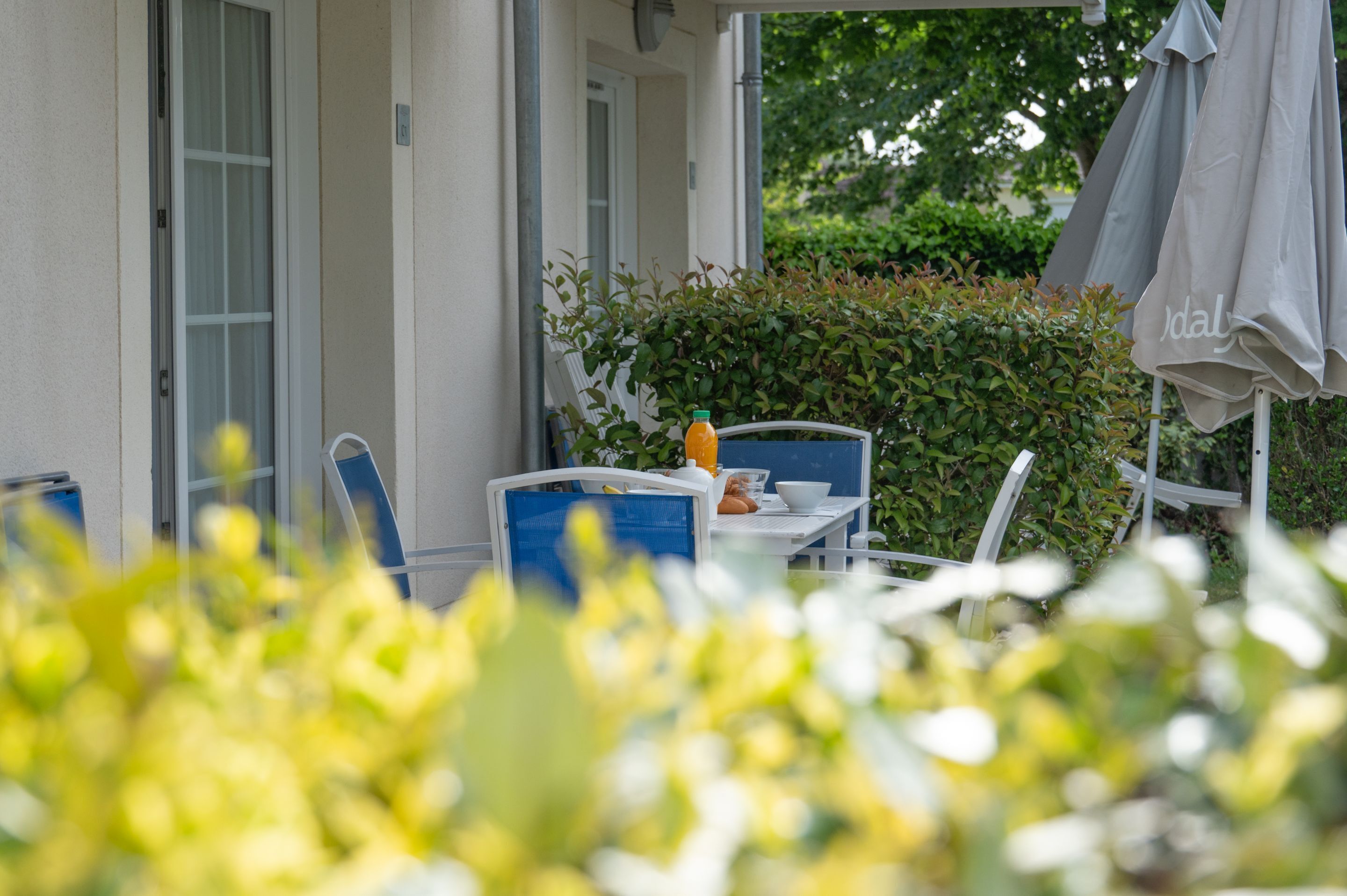 Une terrasse avec une table et des chaises, une bouteille de jus d’orange et un parasol gris.