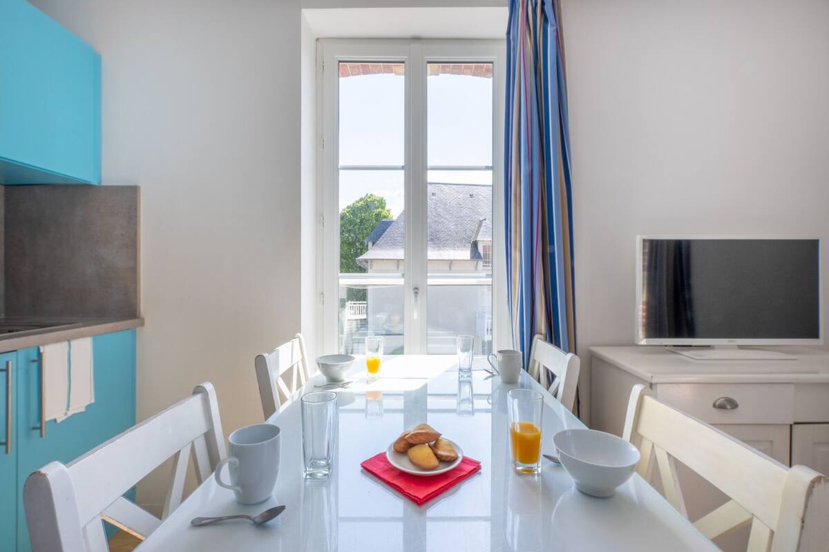 Un coin repas avec une table mise pour le petit-déjeuner, comprenant une assiette de viennoiseries et un verre de jus d’orange.