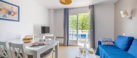 A modern room with a dining table, a sofa, a television, and a window with curtains.