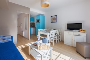 A modern, well-lit room with a bed, a dining table, chairs, a TV, and a kitchen area.