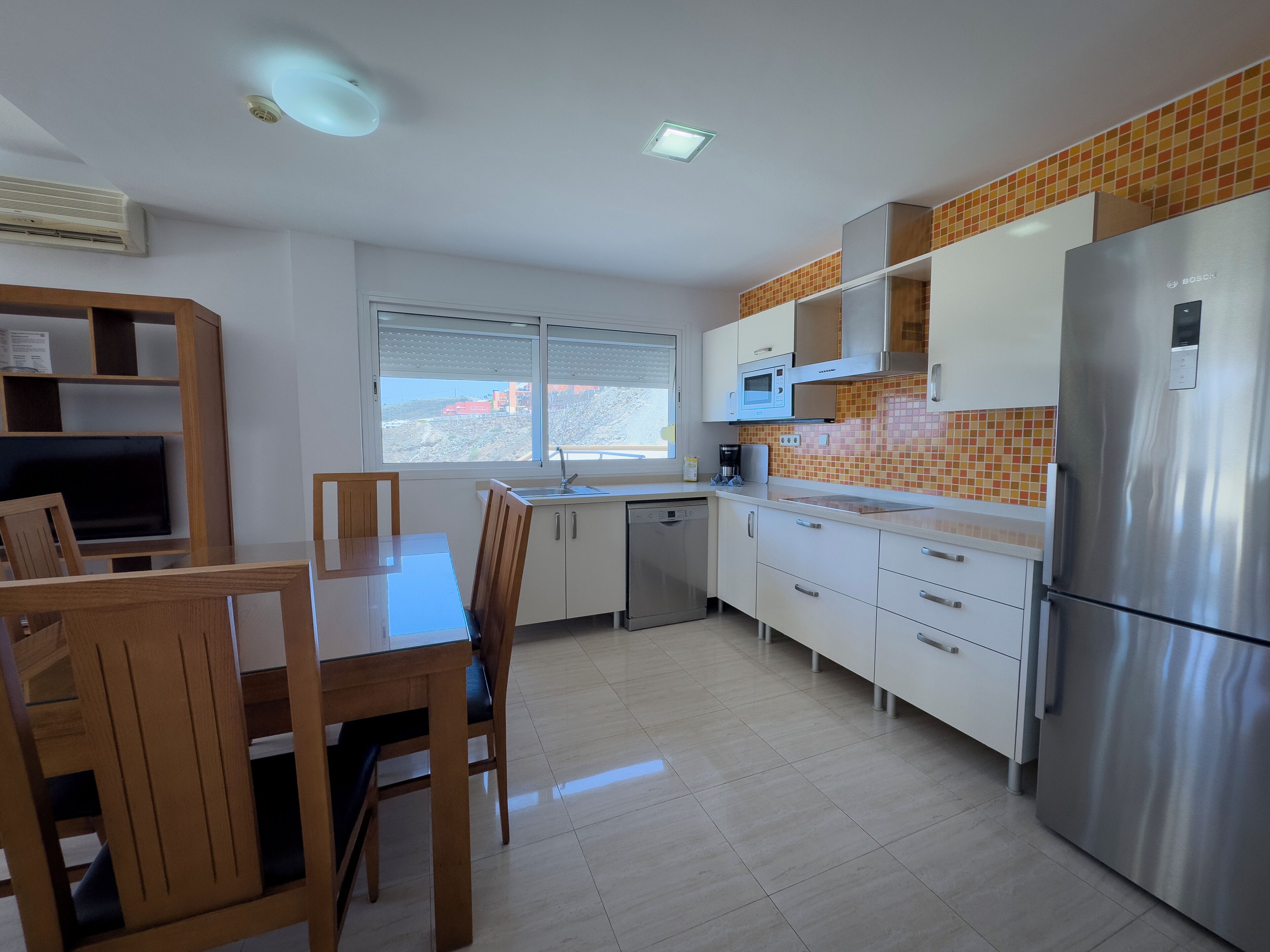 Een moderne keuken met witte kastjes, een roestvrijstalen koelkast en een raam met uitzicht op een gebouw.