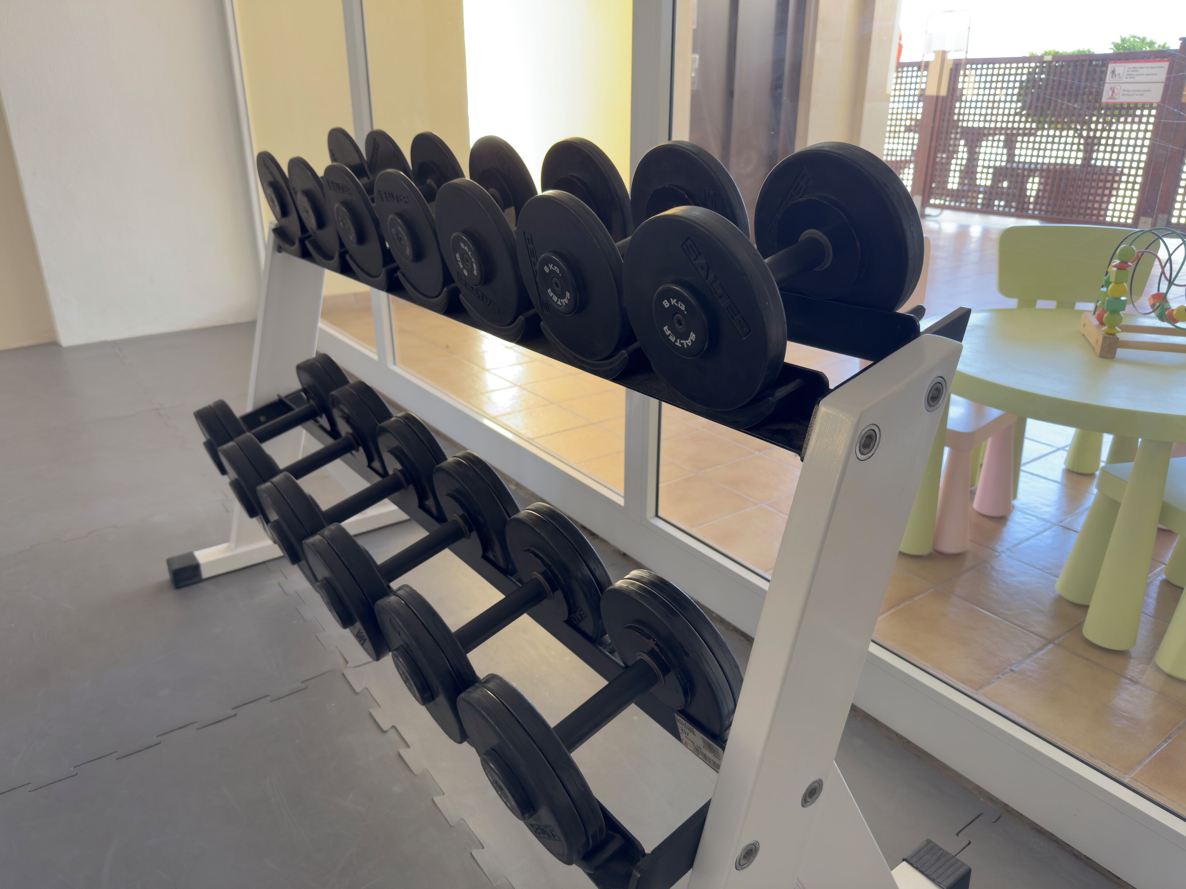 A gym with a rack of dumbbells and a table with children's toys.