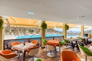 A rooftop dining area with tables and chairs, overlooking a pool and a scenic view. - Holiday Club Sol Amadores (Mogan)