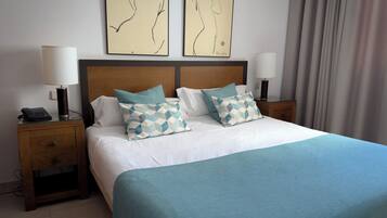 A neatly made bed with two patterned pillows, a wooden headboard, and two bedside tables with lamps.