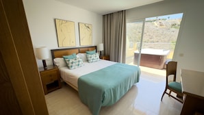 A hotel room with a bed, a nightstand, a desk, a chair, and a balcony with a hot tub. - Holiday Club Sol Amadores (Mogan)