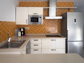 Uma cozinha moderna com armários brancos, uma geladeira de aço inoxidável, micro-ondas e cafeteira.
