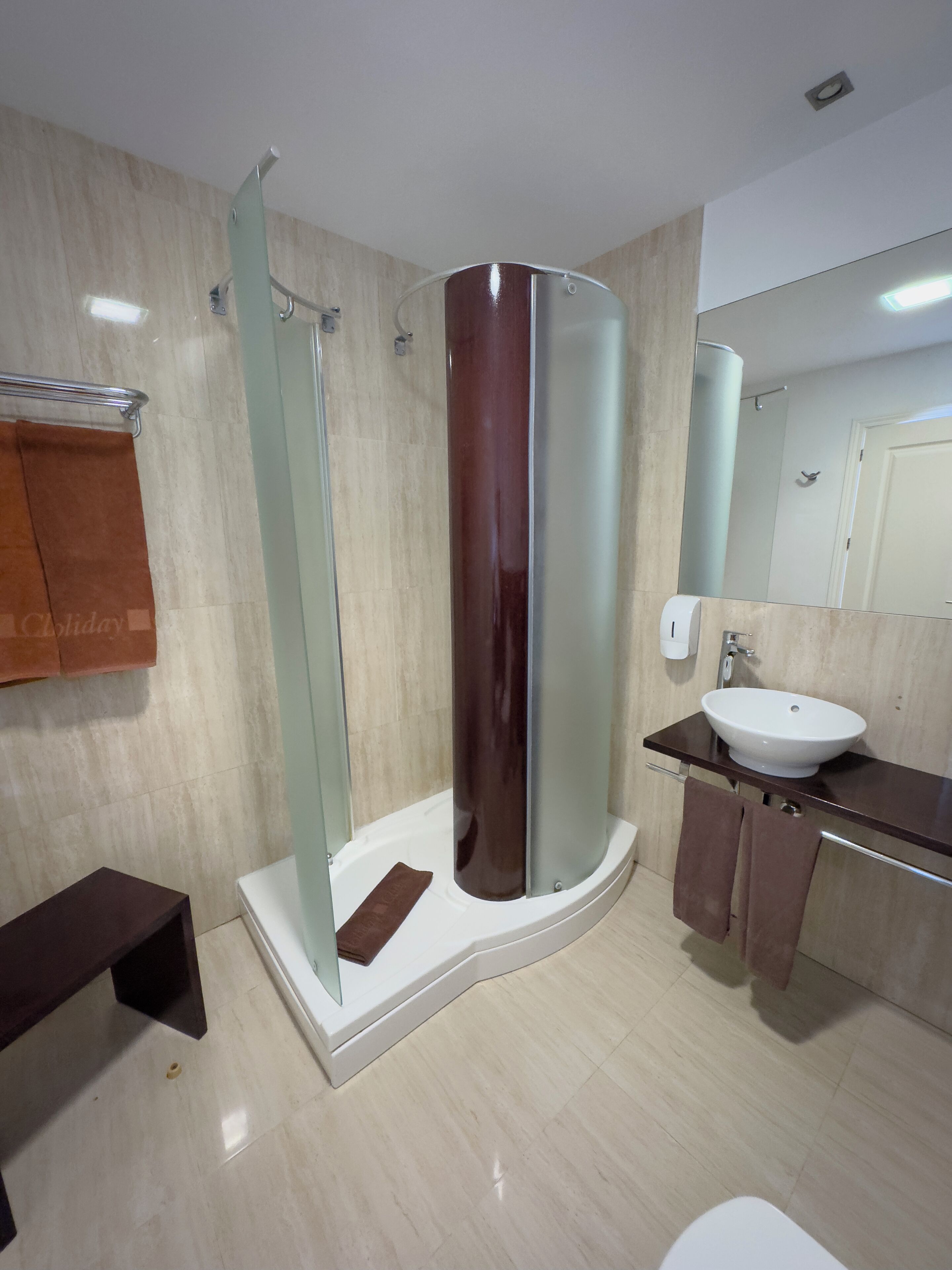 Un baño moderno con cabina de ducha de vidrio, un lavamanos blanco y un mueble de tocador de madera.