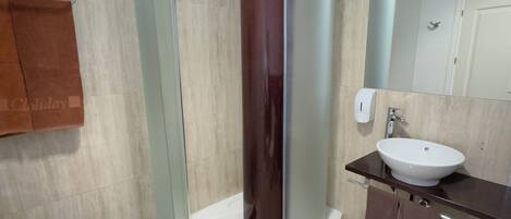 Un baño moderno con cabina de ducha de vidrio, un lavamanos blanco y un mueble de tocador de madera.