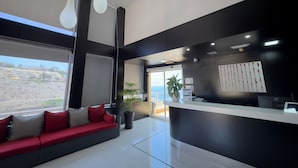 A modern reception area with a black and white color scheme, a reception desk, a seating area with a red sofa, and a large window offering a view of the landscape. - Holiday Club Sol Amadores (Mogan)