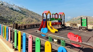 A playground with a slide and climbing structures, set against a hillside backdrop. - Holiday Club Sol Amadores (Mogan)