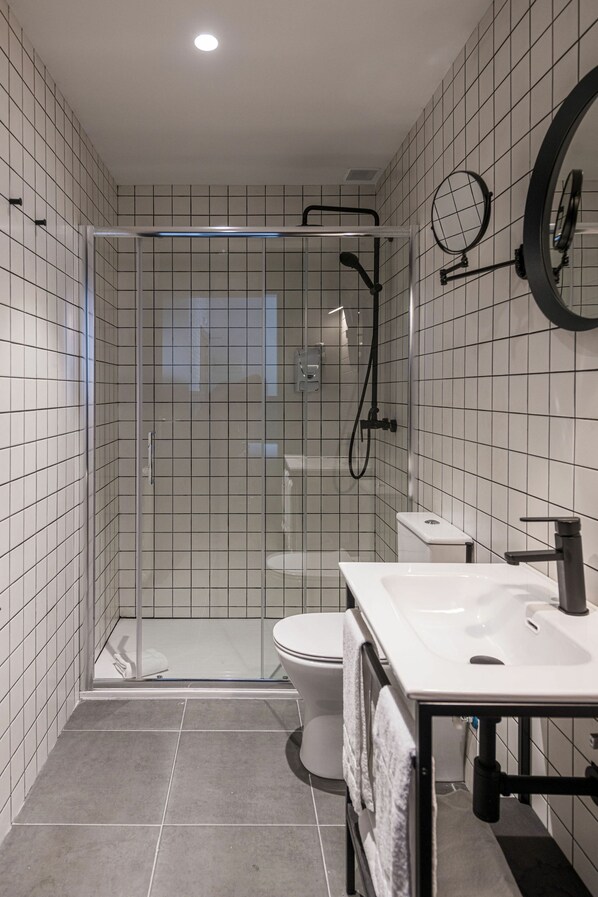 A modern bathroom with a glass-enclosed shower, a white toilet, and a sink with a towel rack.