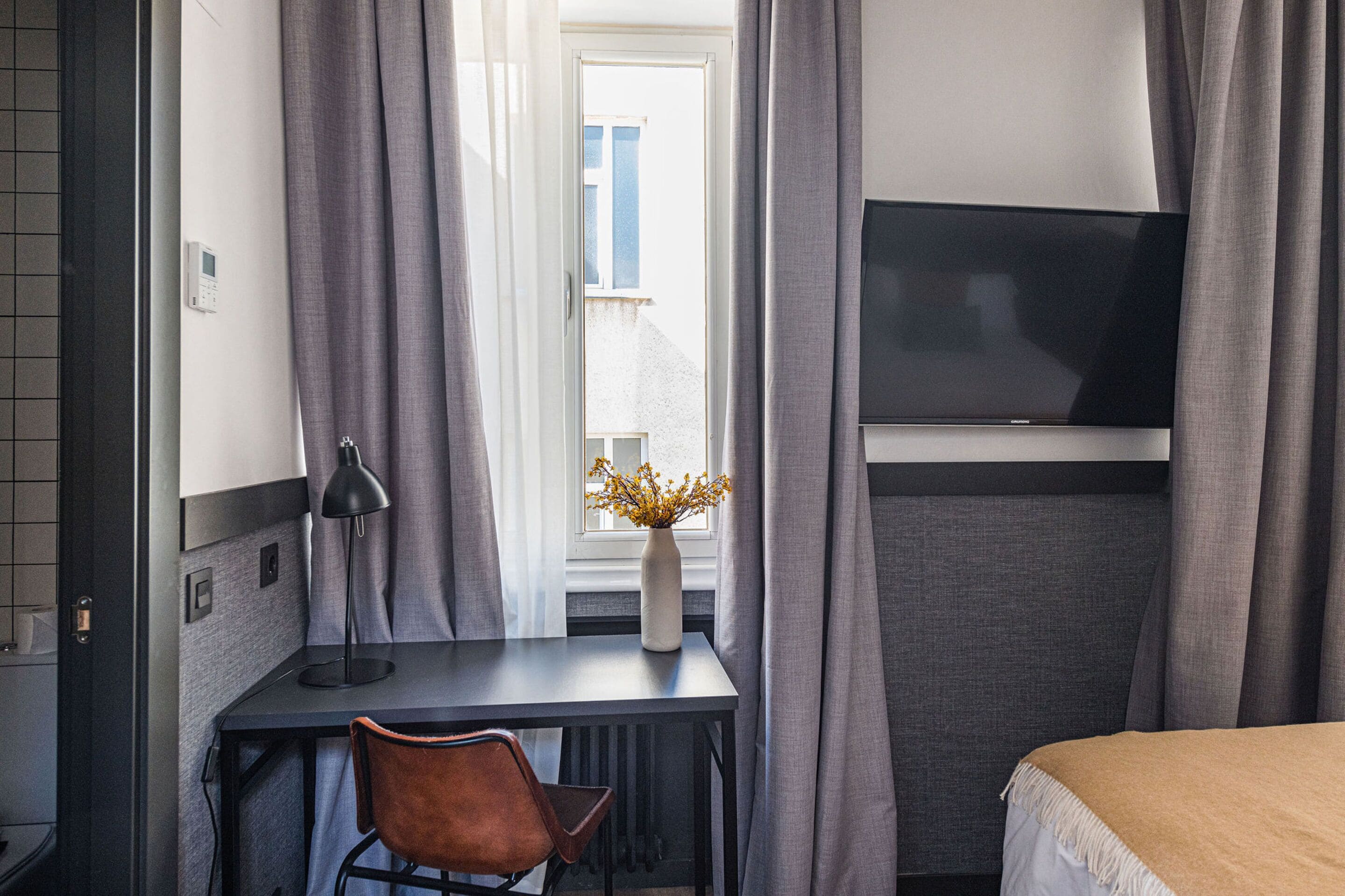 A hotel room with a desk, chair, TV, and a bed.