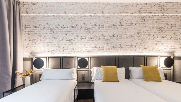 A hotel room with two beds, a brick-patterned wall, and a modern design. - BYPILLOW San Mamés (Bilbao)