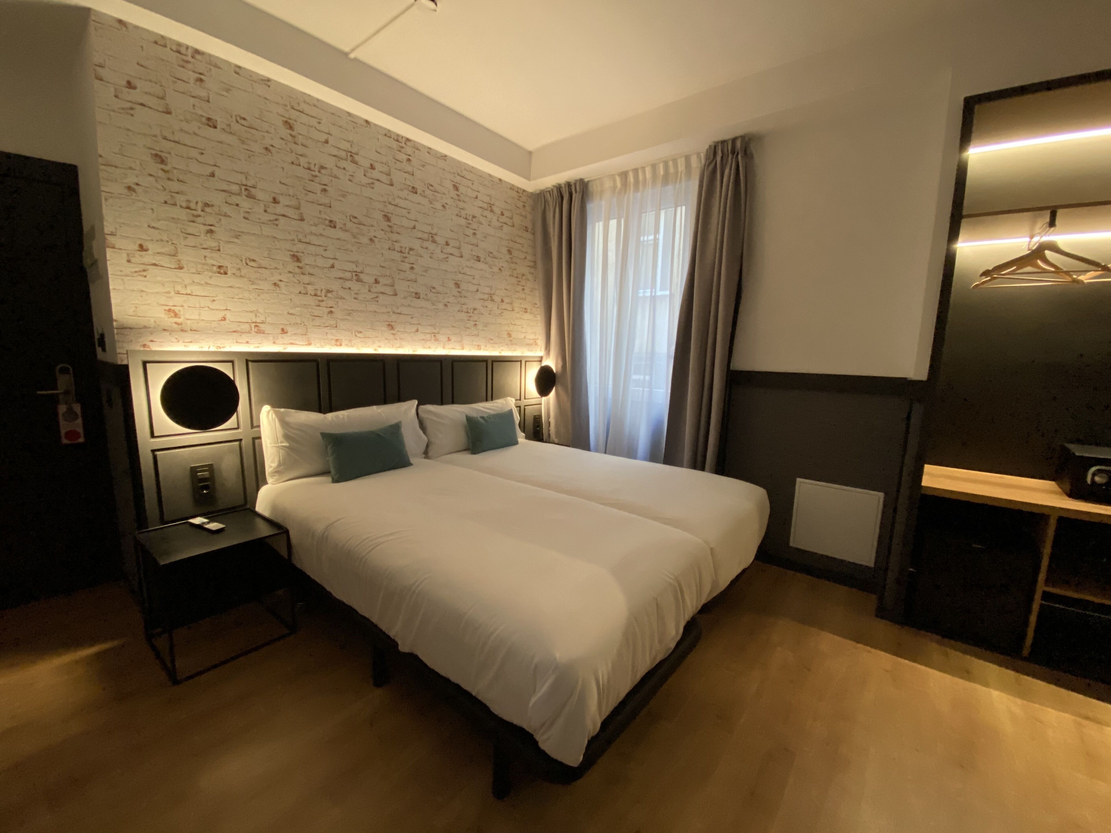 Een hotelkamer met een groot bed, een ronde spiegel boven het bed, een kledingkast met kledingroede, en een metselwerk muur.