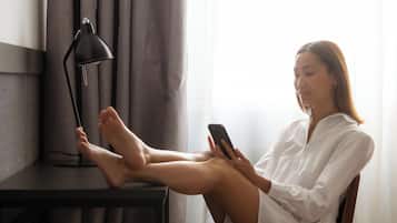 A person sitting on a chair at a desk with a lamp, using a smartphone.