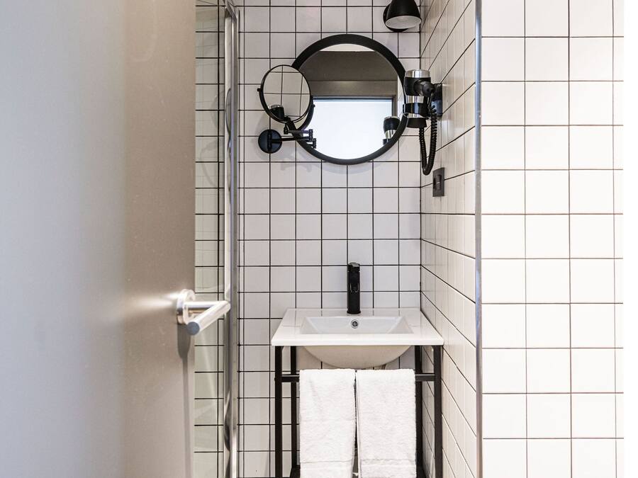 Un bany compacte amb una cabina de dutxa de vidre, un lavabo blanc i un mirall a la part superior.