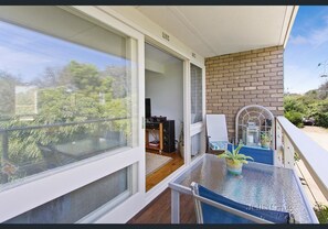 A balcony with a glass table, a chair, and a view of a garden and trees. - Bayside St Johns Close (Blairgowrie)