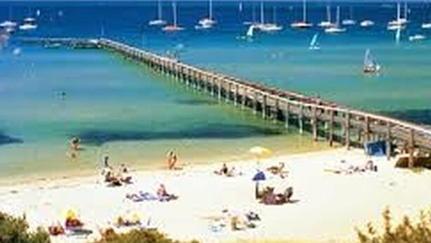 Eine Pier, die sich in ein klares, blaues Meer erstreckt, mit mehreren Booten in der Nähe, die vor Anker liegen.