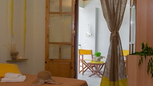 Um quarto com cama, porta de madeira, uma mesinha com cadeira e cortina.