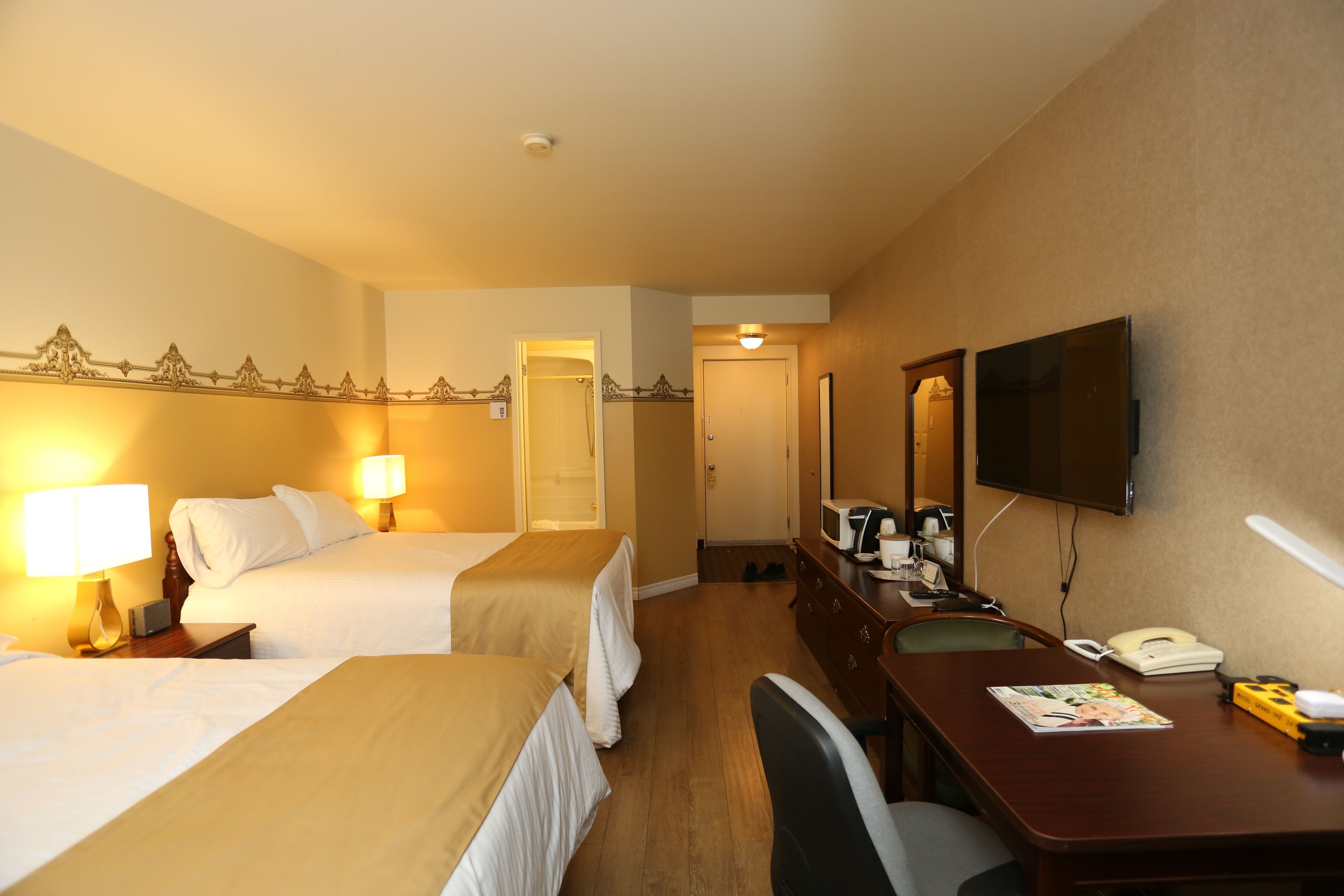 A hotel room with two beds, a desk with a telephone, a television, and a mirror.