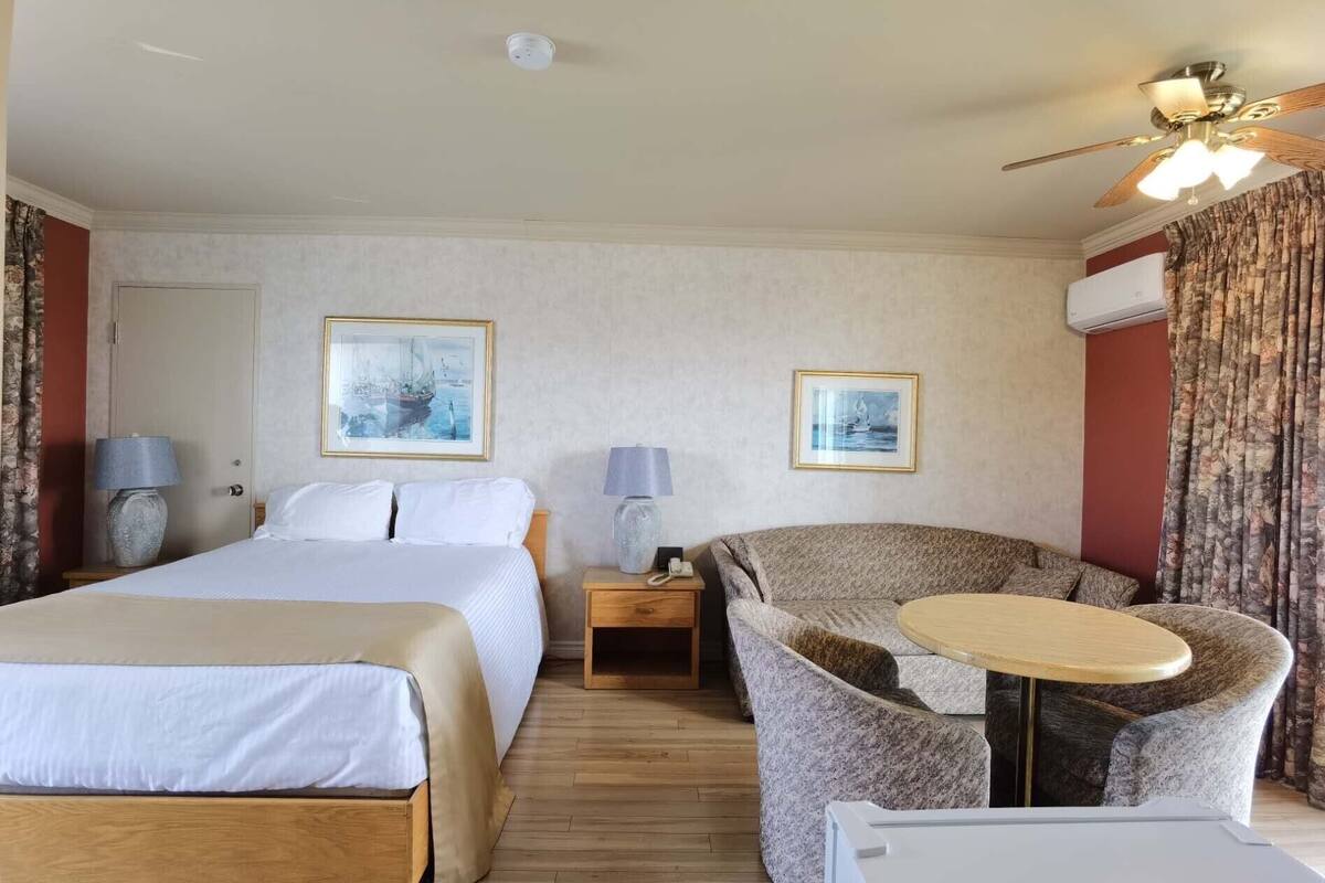 A hotel room with two beds, a chair, a small table, and two lamps.