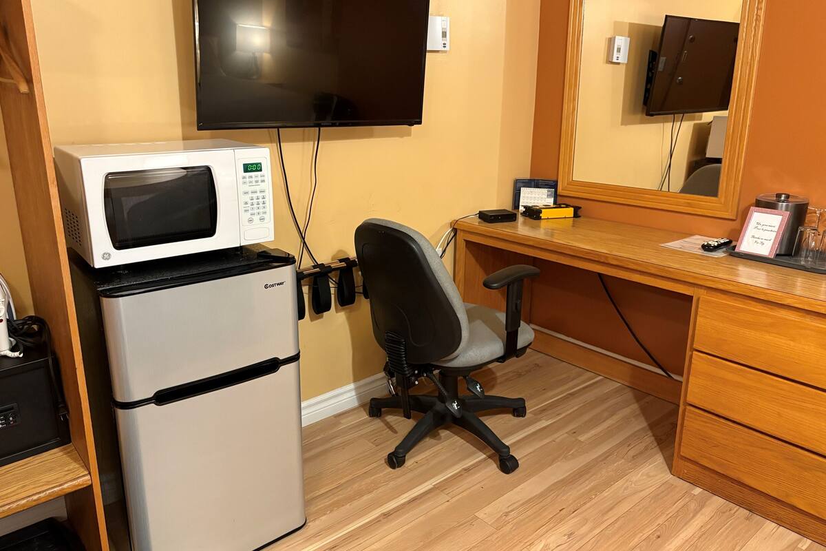 A compact kitchenette with a microwave, refrigerator, and a small desk with a chair.