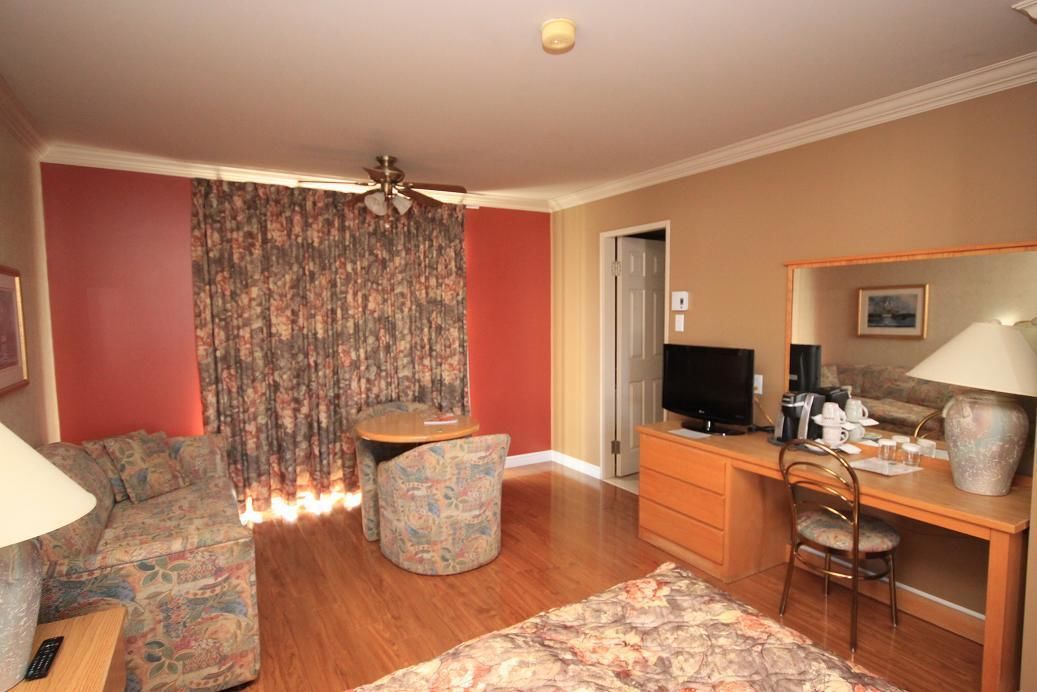 Habitación de hotel con sofá, una mesita, escritorio con silla, televisor y ventilador de techo.