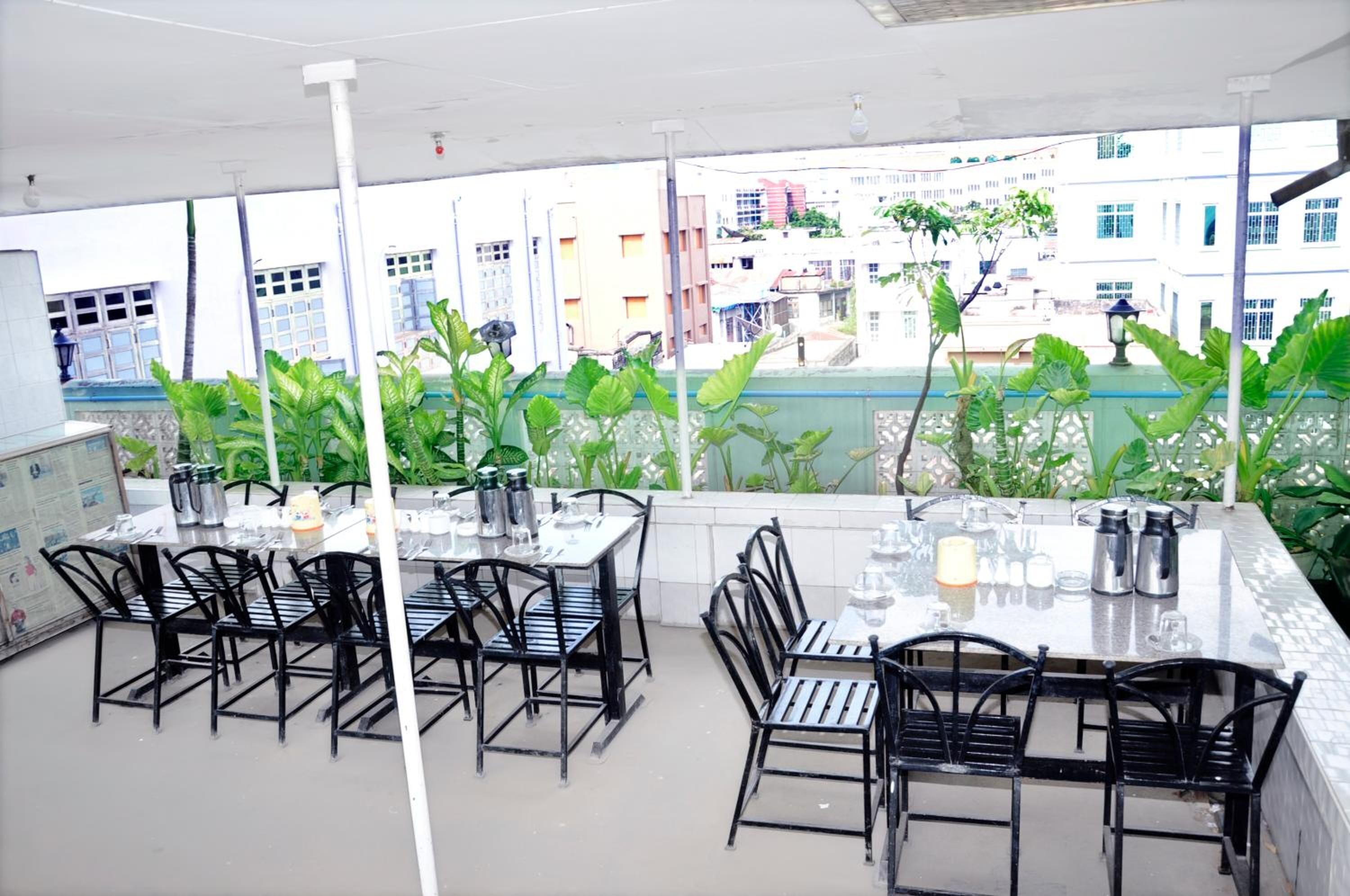 A rooftop terrace with tables and chairs, surrounded by greenery and overlooking a cityscape.