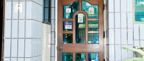 A hotel entrance with a tiled facade, a wooden door with a glass panel, and a 'dot' sign.
