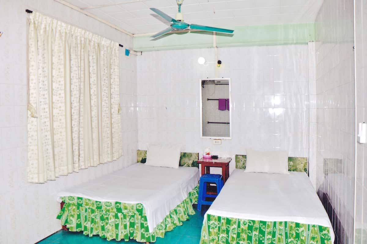 A room with two beds, a ceiling fan, a small table, and a mirror on the wall.