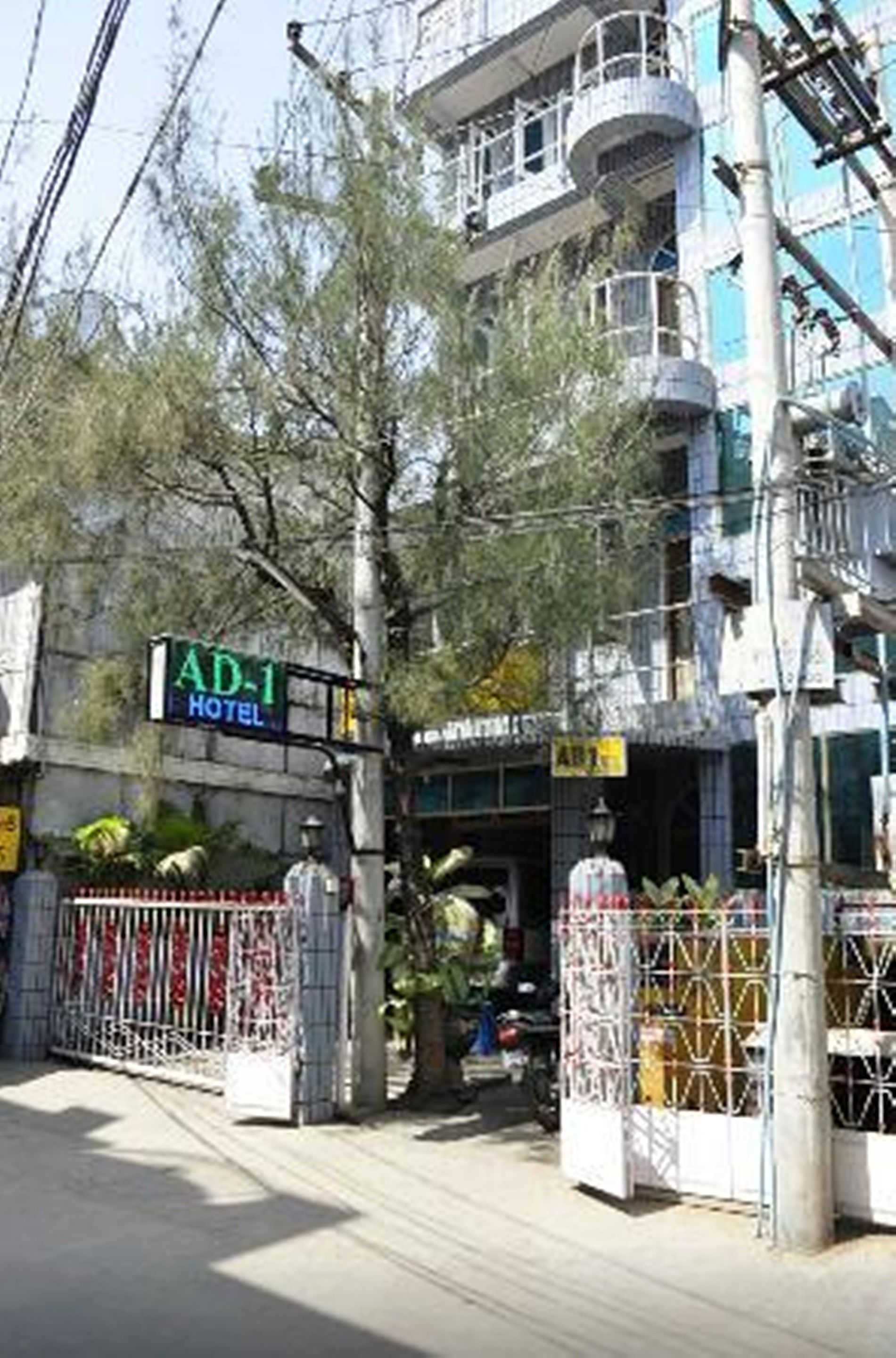 Entrada de un hotel con un camino de acceso porticado, un cartel que dice 'AD-1 Hotel' y un edificio con balcones.