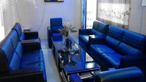 A living room with blue sofas, a coffee table, and a TV mounted on the wall. - Red Dragon Hotel Hsipaw (Hsipaw)