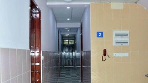 A hallway with a checkered floor, a door on the left, and a wall with a number sign and a fire alarm on the right. - Red Dragon Hotel Hsipaw (Hsipaw)