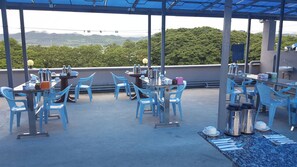 An outdoor dining area with blue chairs and tables, overlooking a mountainous landscape.
