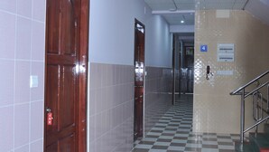 A hallway with checkered flooring, a wooden door, and a staircase with a metal railing. - Red Dragon Hotel Hsipaw (Hsipaw)