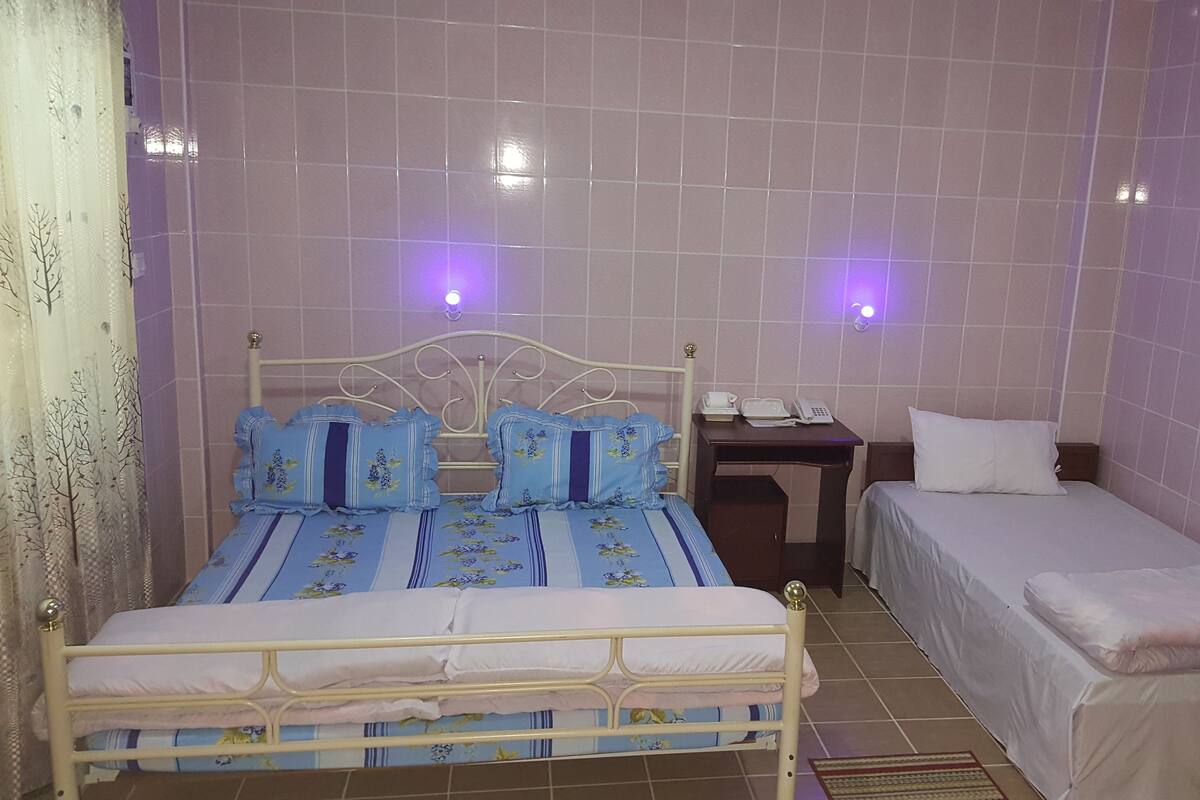 A room with a bed, a bedside table with a phone, and a small table with a lamp.