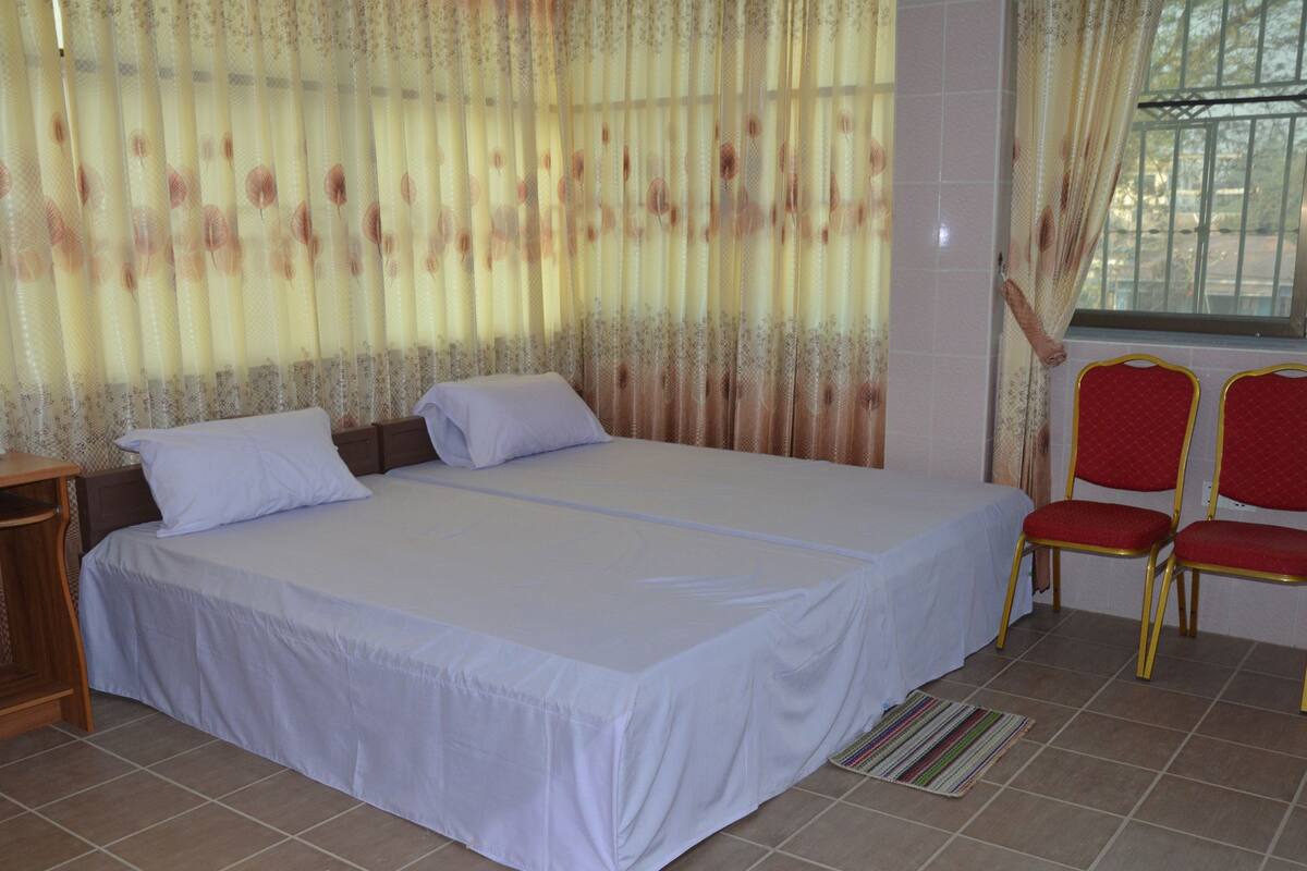 A hotel room with a bed, two chairs, a desk, and a window with curtains.