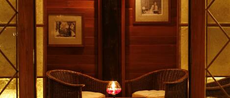 A traditional room with wooden walls, a central pillar, two wicker chairs, a chessboard, and framed pictures on the walls.
