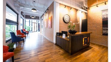 A reception area with a wooden reception desk, a clock, and a plant. There are red and blue chairs in the background.