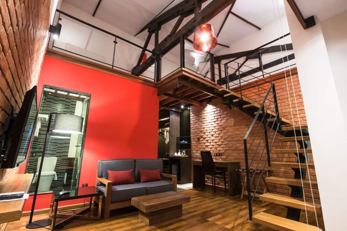 A modern living room with a red accent wall, a wooden staircase, and a glass partition.