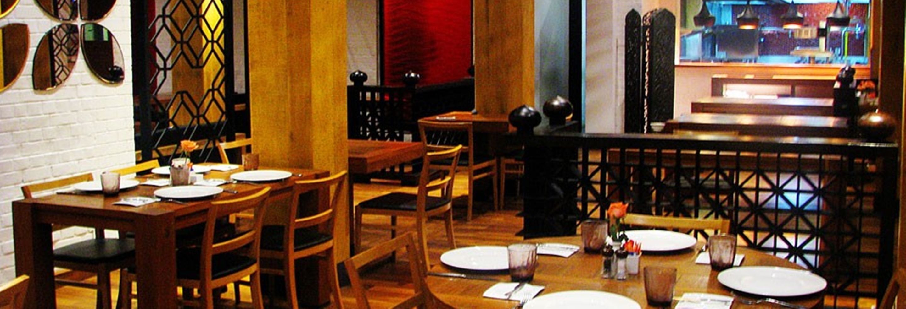 A restaurant with wooden tables and chairs, a brick wall, and a decorative metal partition.
