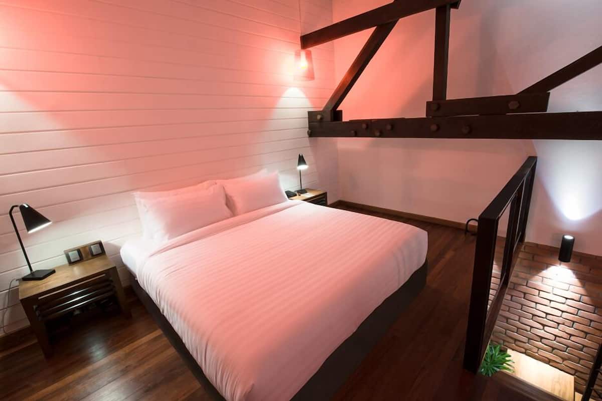A bedroom with a bed, nightstands, a lamp, and a wooden staircase.