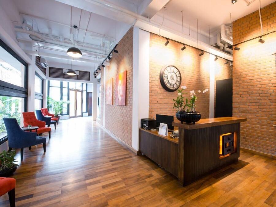 A reception area with a wooden reception desk, a clock, and a plant. There are red and blue chairs along the wall.