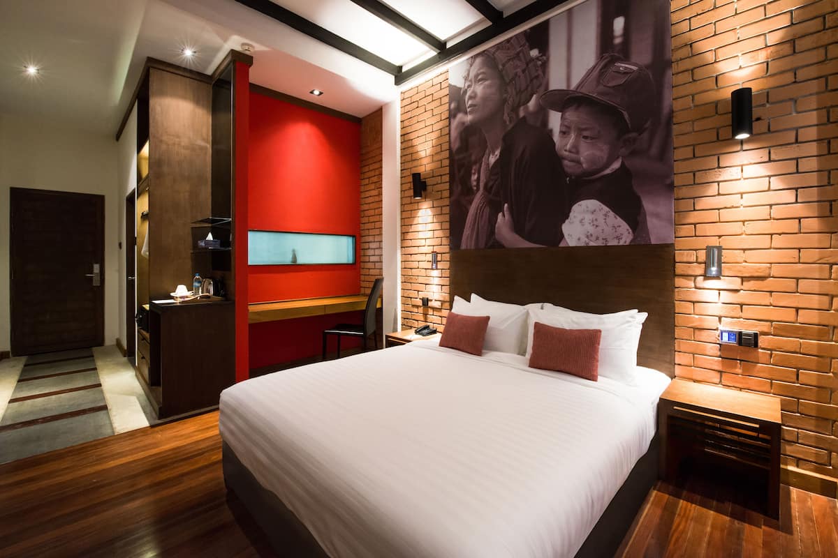 A hotel room with a large bed, a red accent wall, a brick wall, and a poster.