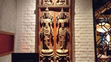 A carved wooden panel with two figures, set against a brick wall.
