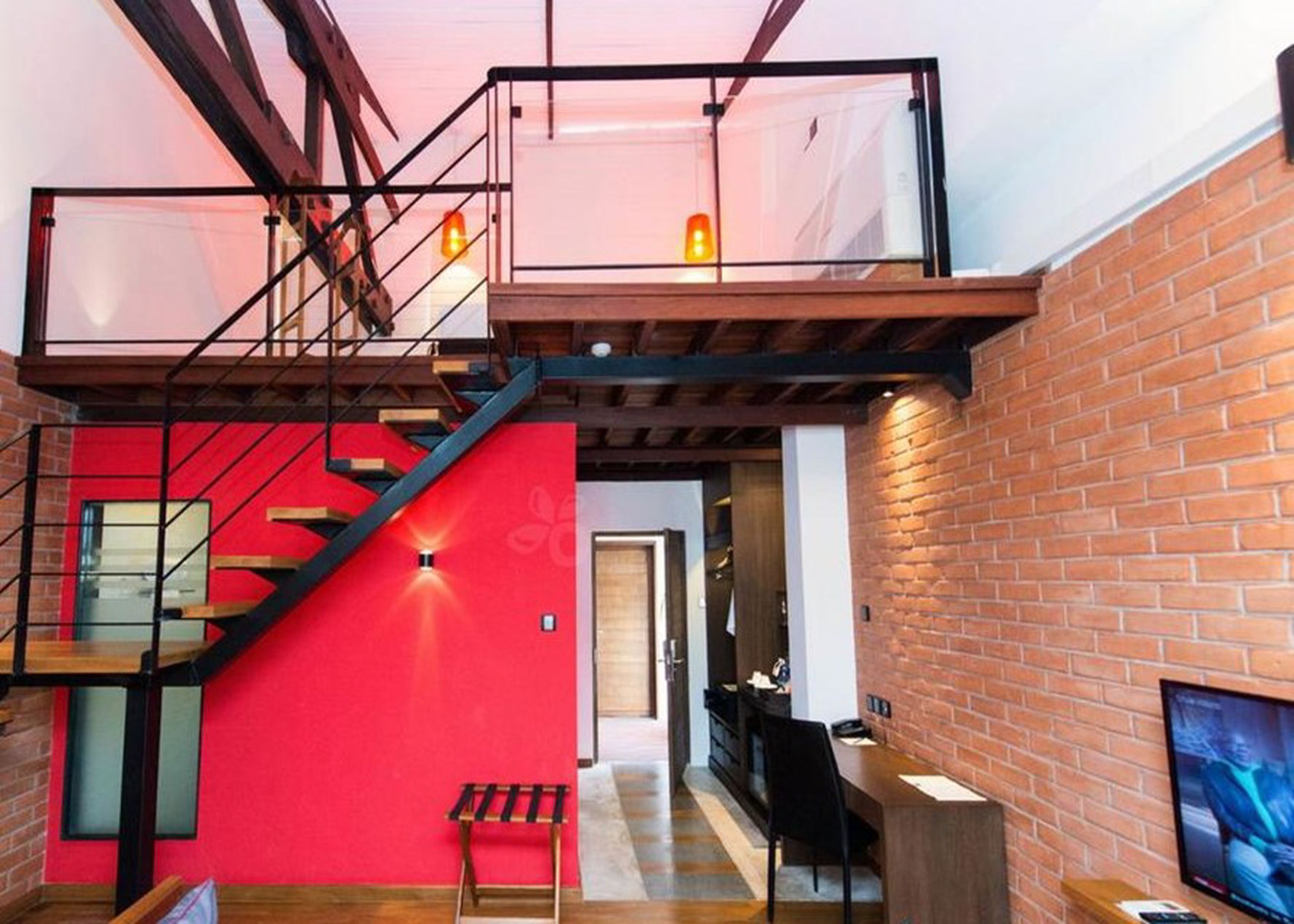 A multi-level interior with a staircase, a red wall, a wooden bench, and a TV mounted on the brick wall.