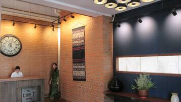 A hotel reception area with a brick wall, a large clock, a patterned tapestry, and a reception desk labeled "The Loft Hotel".
