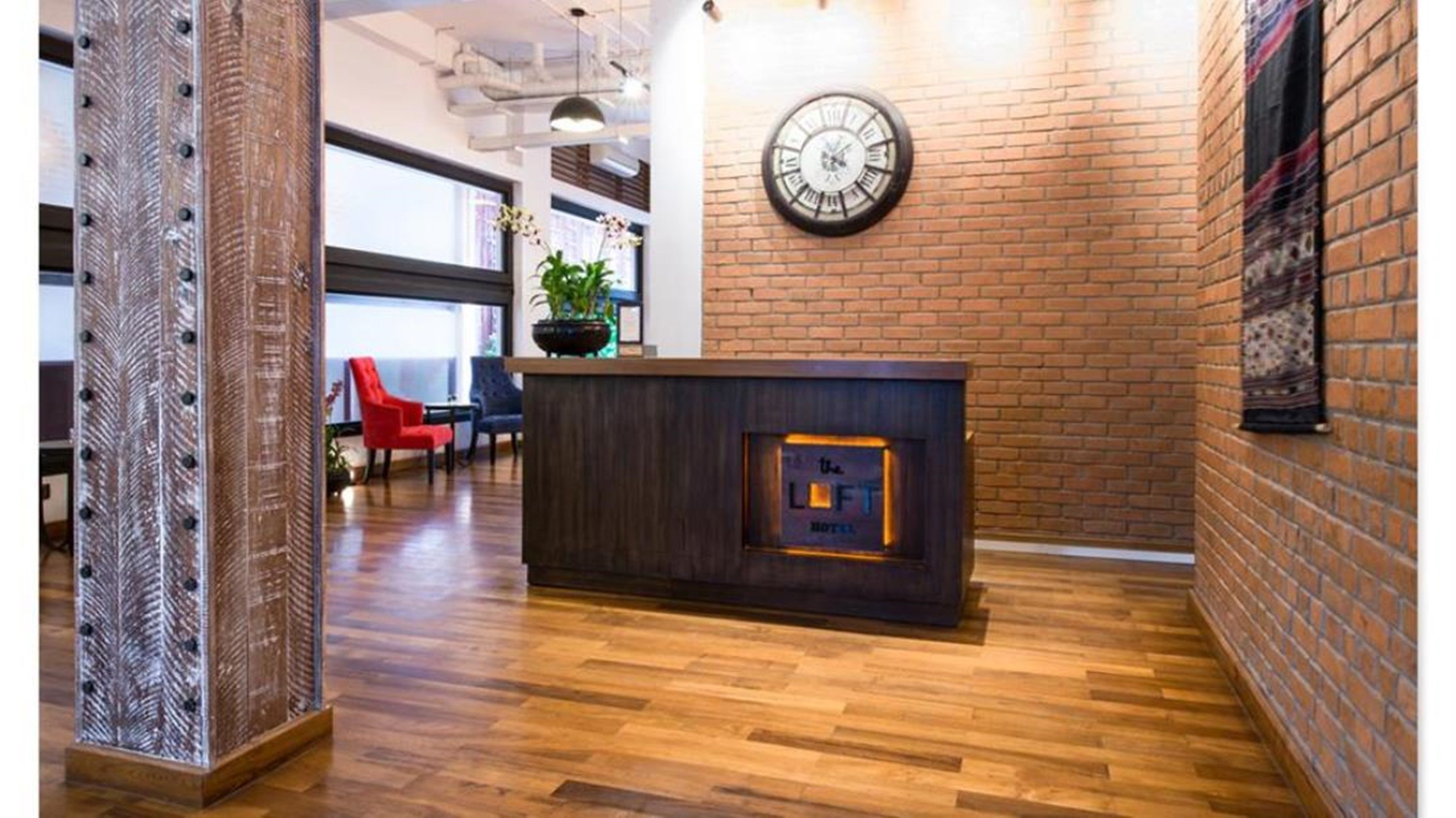Un mostrador de recepción con un reloj, una planta en maceta y una silla roja al fondo.