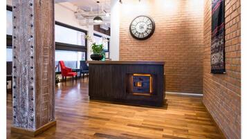 Un mostrador de recepción con un reloj, una planta en maceta y una silla roja al fondo.